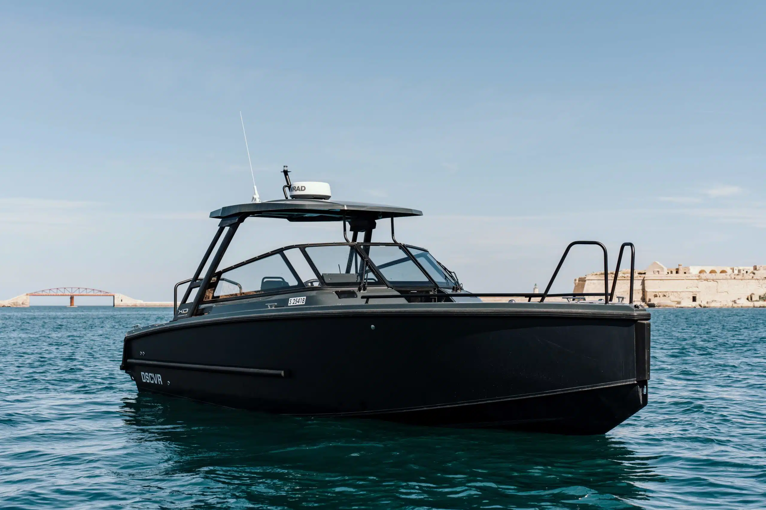 Bild av XO DSCVR 9 T-top Black-bten som kryssar p vattnet, med dess eleganta och moderna design, kraftfulla motor och bekvma sittplatser fr passagerare.